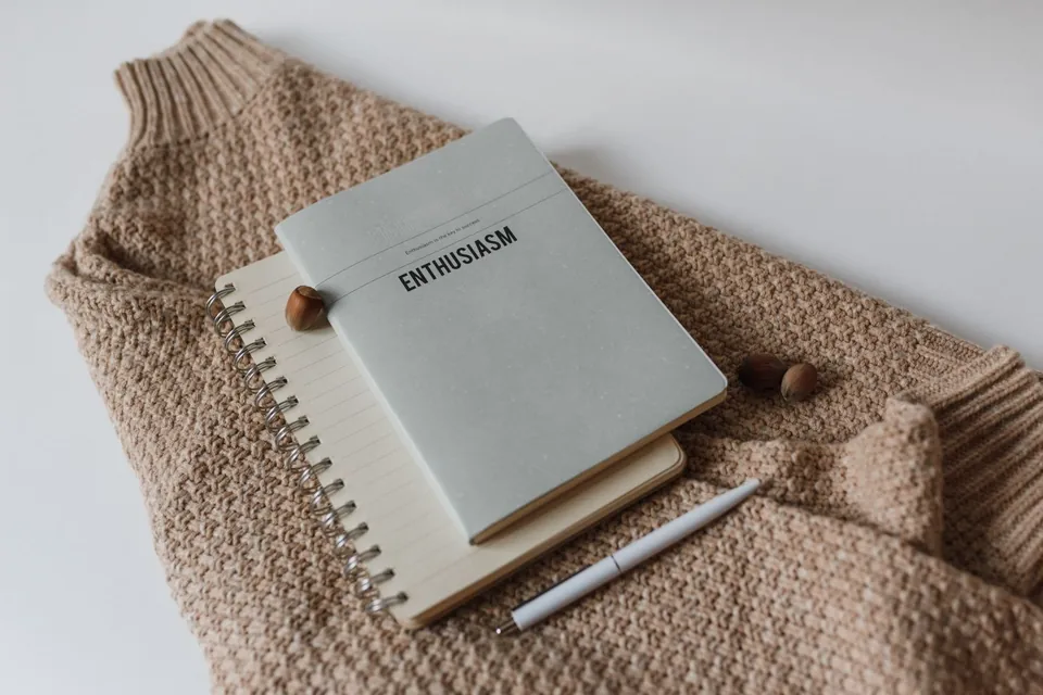 Miękki beżowy sweter z wyraźną fakturą splotu i notesem — fotografia ilustracyjna